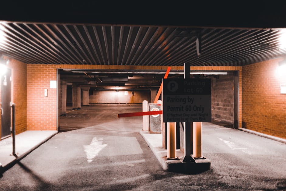 An underground parking garage entrance inside a residential building, featuring brick walls on either side and a dark, wooden slatted ceiling. A park entry barrier with an orange arm is positioned acr